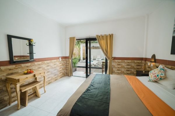 Cozy tropical bedroom with wooden bed, orange bedding, fruit bowl on rustic table, and sliding doors to garden patio.